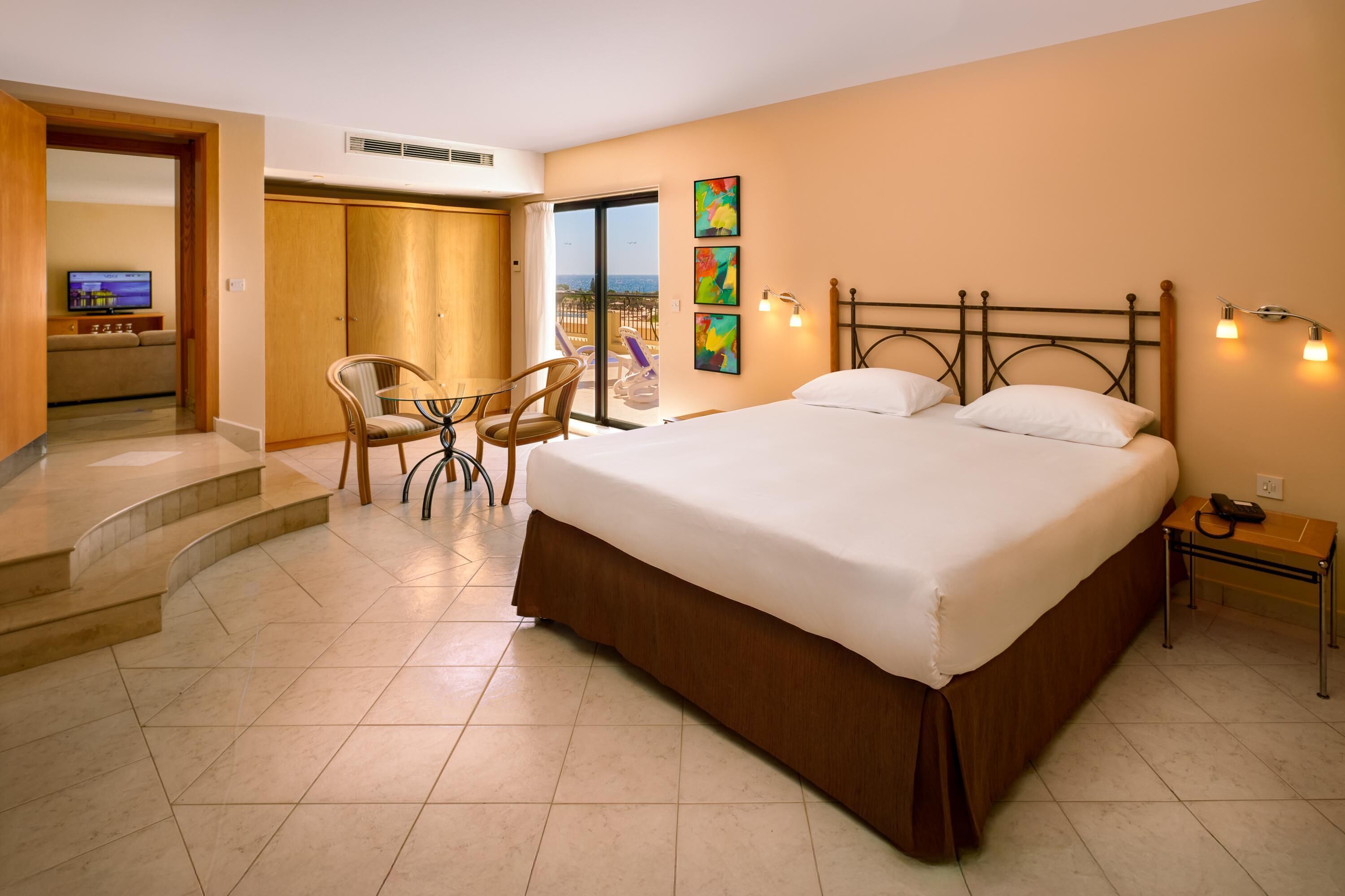 A hotel room with a large bed, a desk with a chair, a TV, and a balcony with a view.