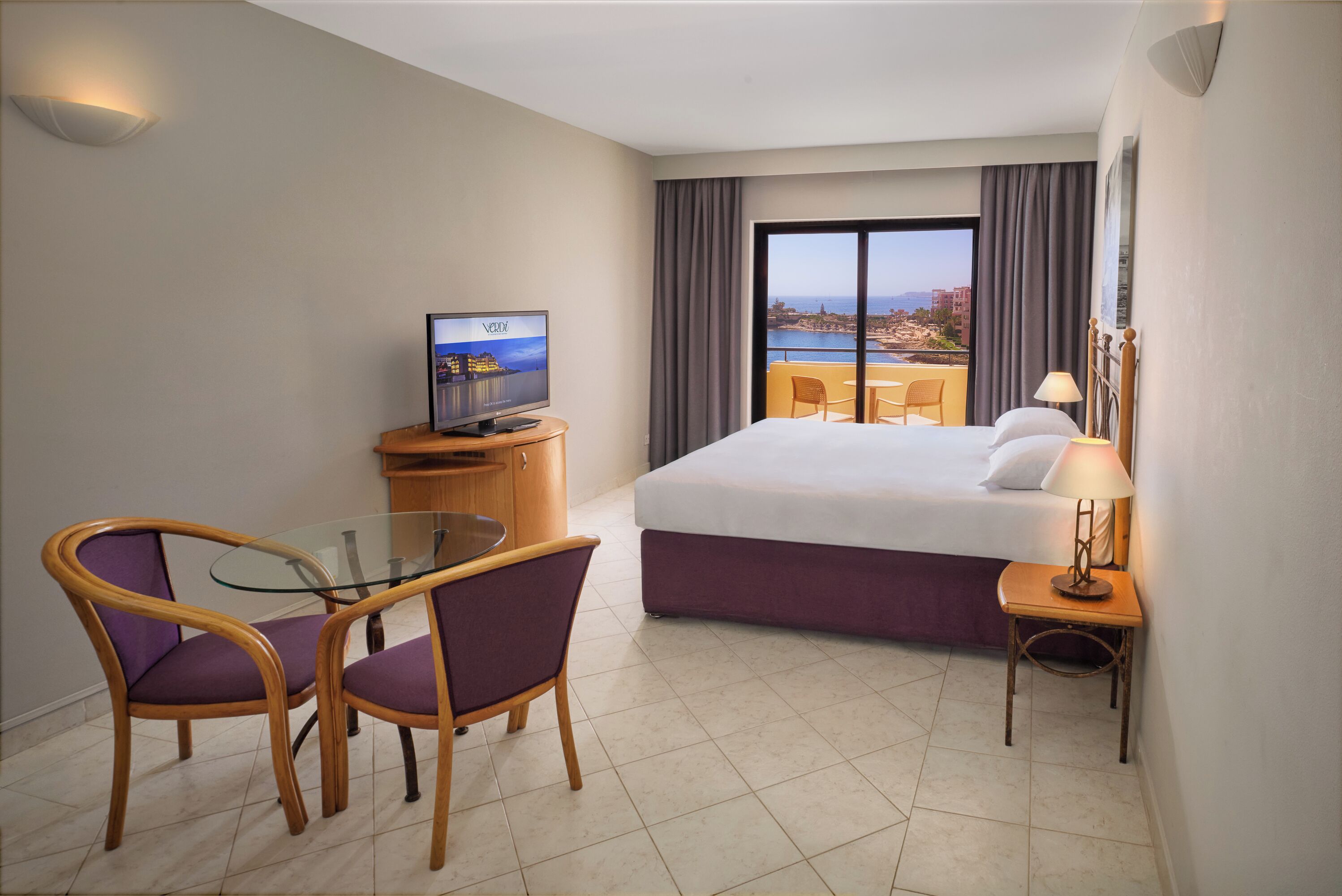 Une chambre d’hôtel avec un lit, une télévision, une table en verre avec des chaises, une lampe et une vue sur la ville.