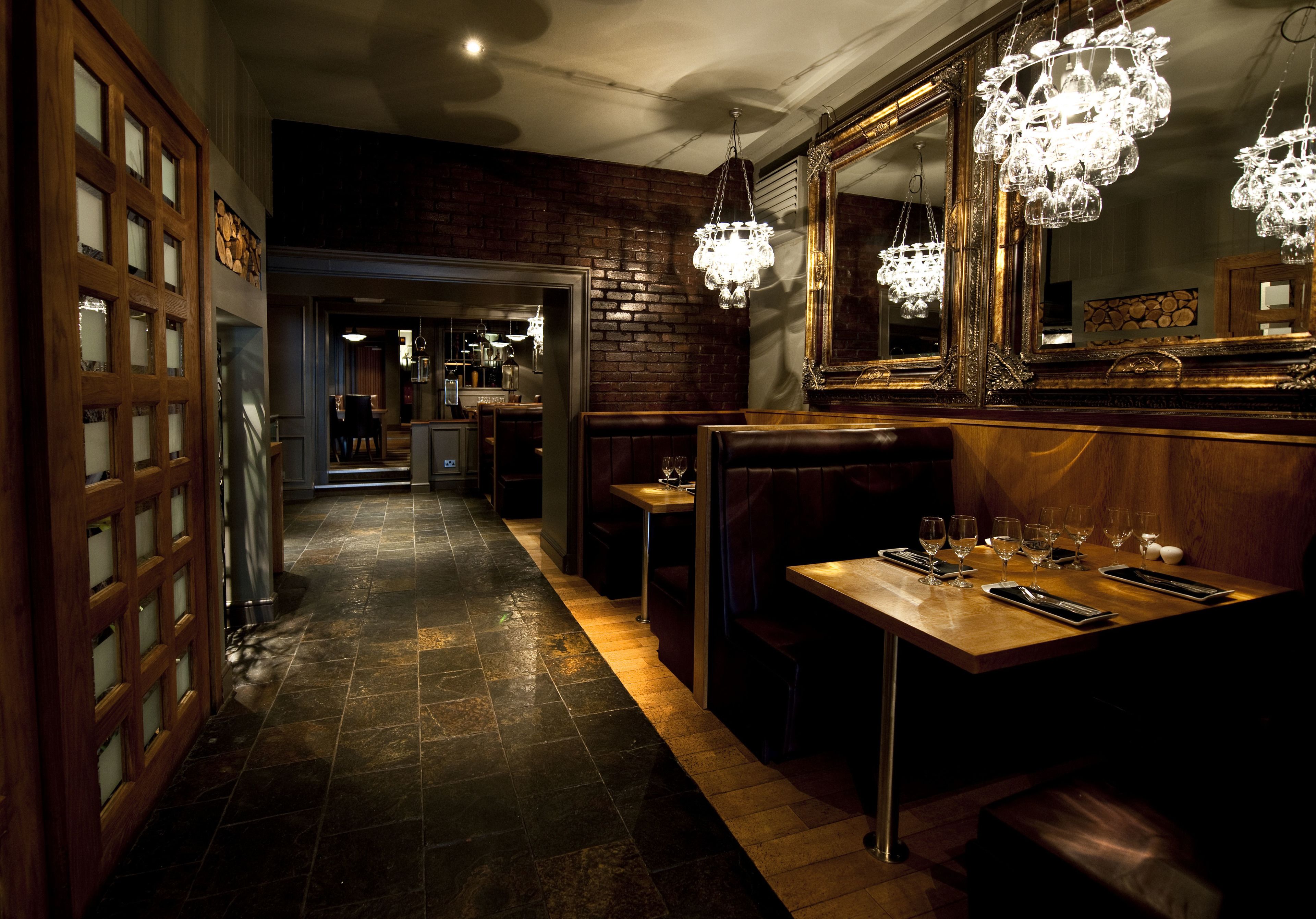 A dimly lit restaurant with a brick wall, wooden flooring, and a large mirror above a wooden table set for dining.
