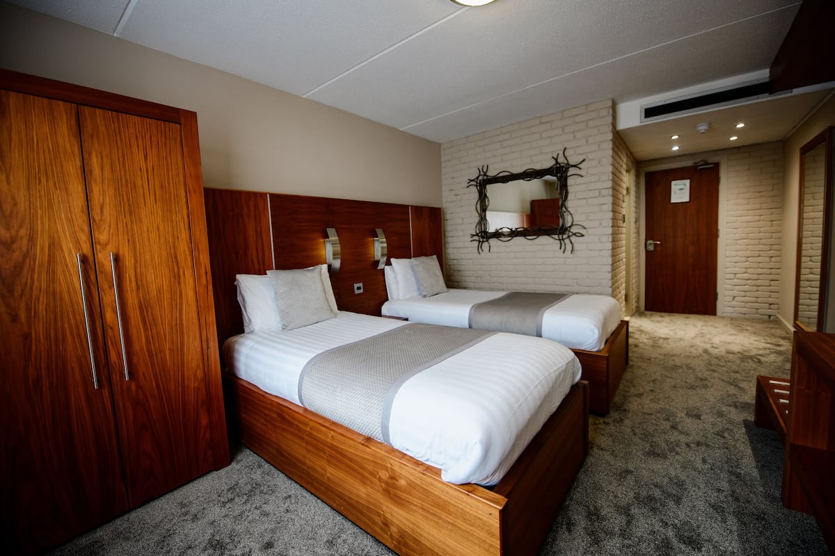 A hotel room with two single beds, a wooden wardrobe, a mirror, and a brick wall.