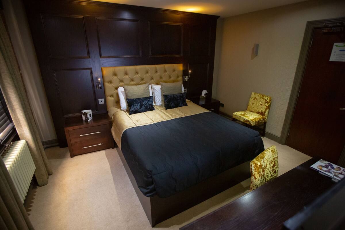 A hotel room with a large bed, a nightstand, a chair, and a wooden headboard.