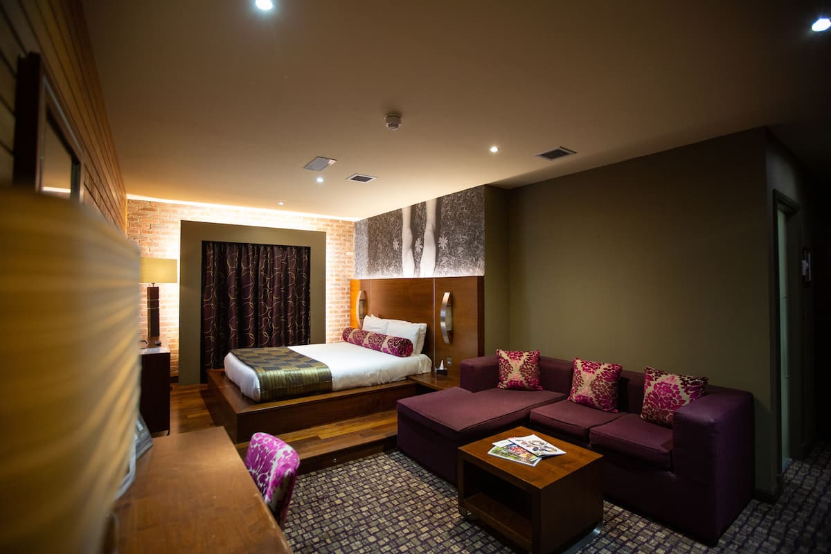 A hotel room with a bed, a sofa, a wooden coffee table, and a patterned carpet.