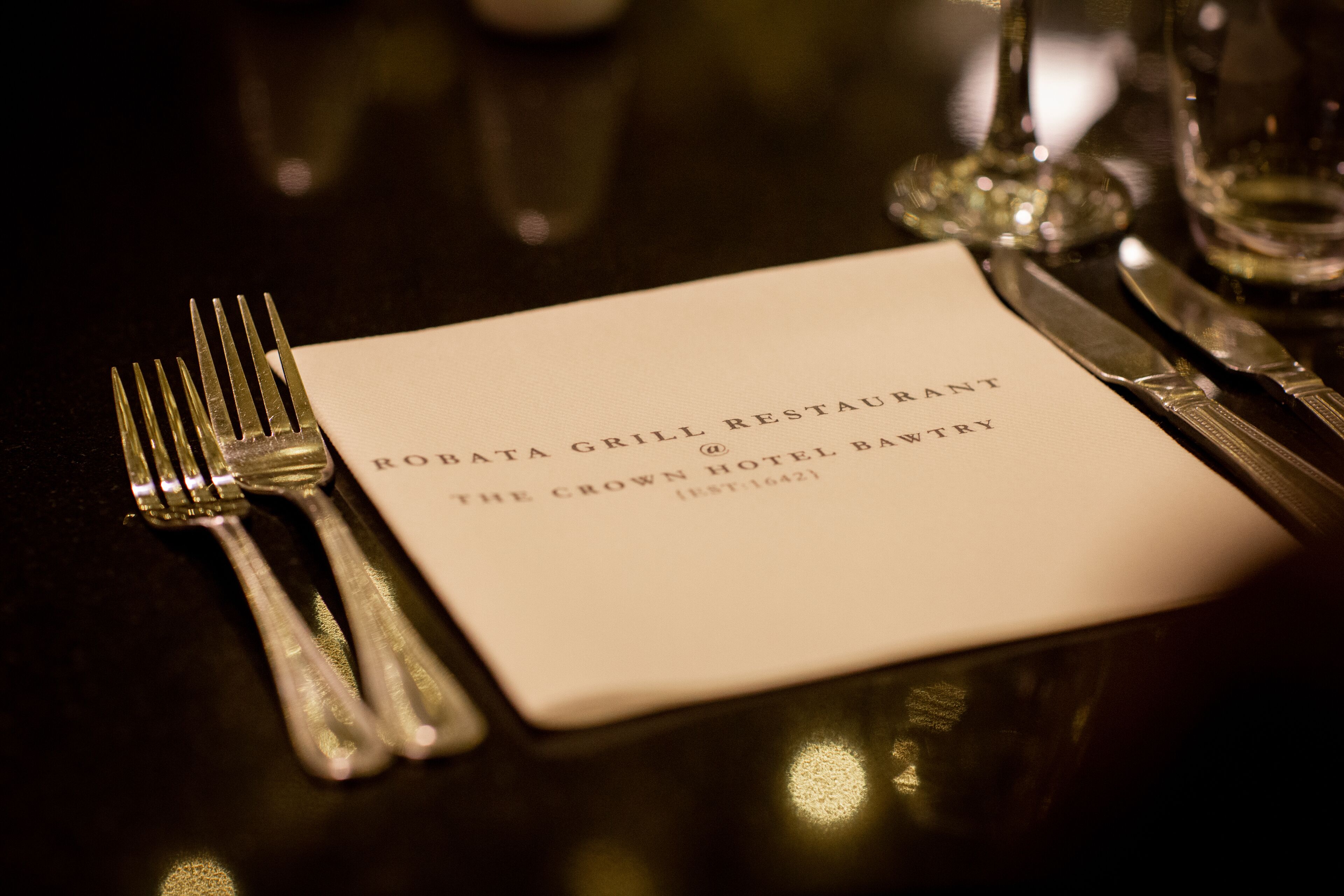 A table setting with a menu card, cutlery, and a glass.