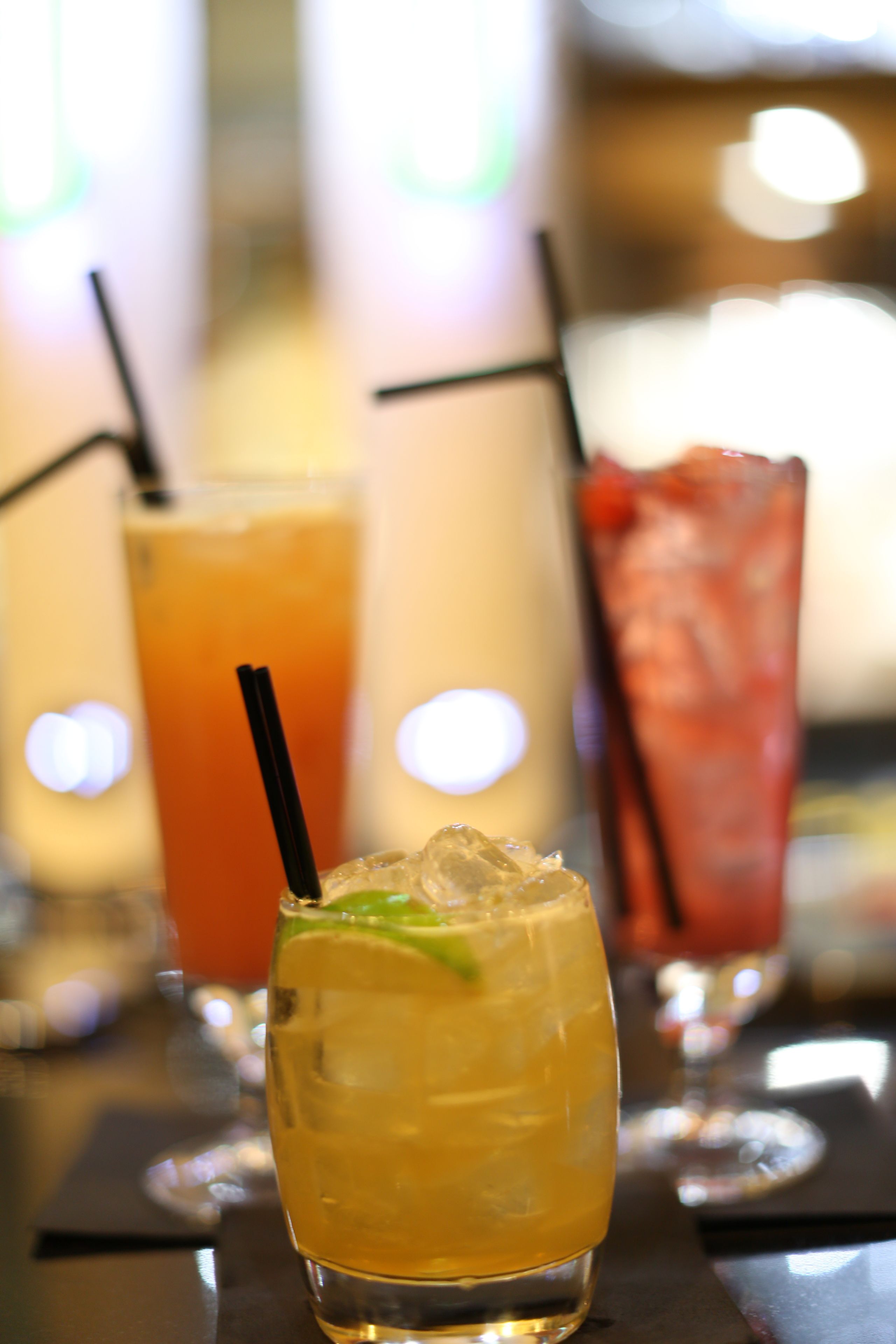 A bar setting with three glasses of beverages, each with a straw.