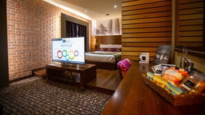 A hotel room with a brick wall, a bed, a television, a wooden desk, and a basket of toiletries. - The Crown Hotel Bawtry, Doncaster (Doncaster)