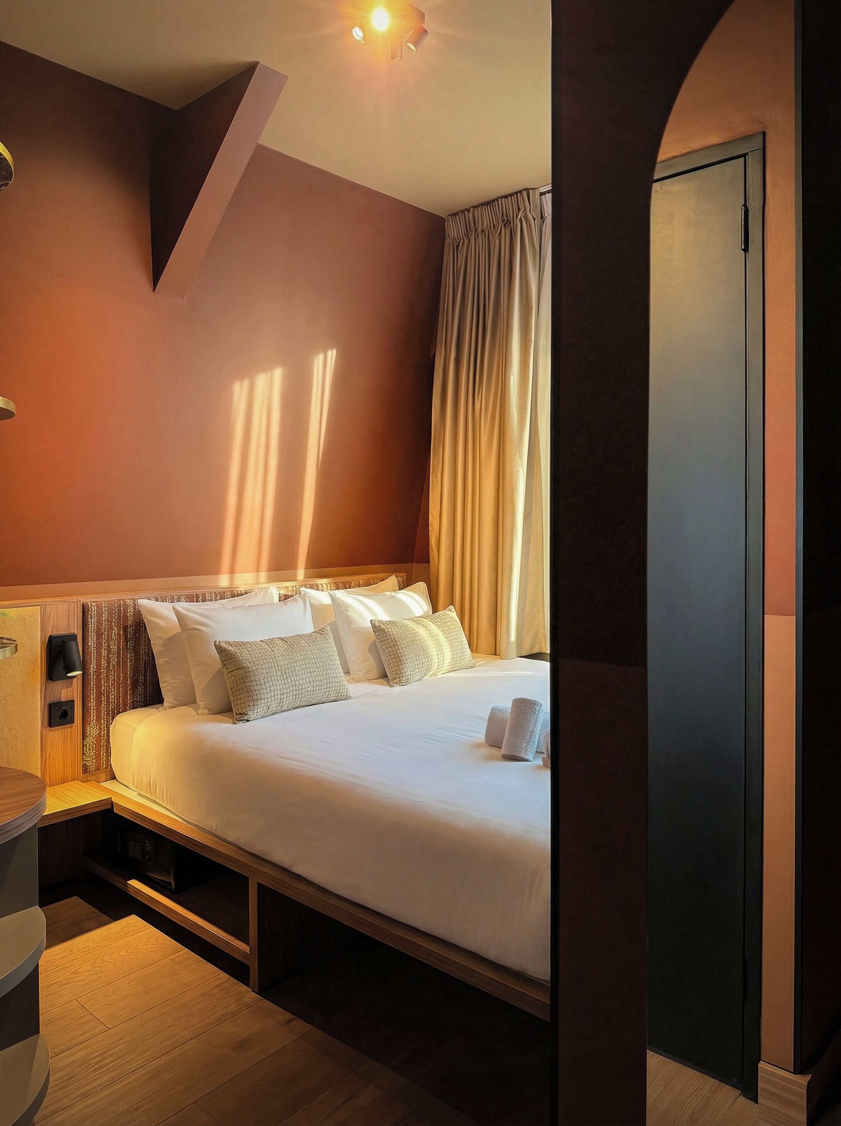 A hotel room with a bed, bedside table, and a wardrobe.