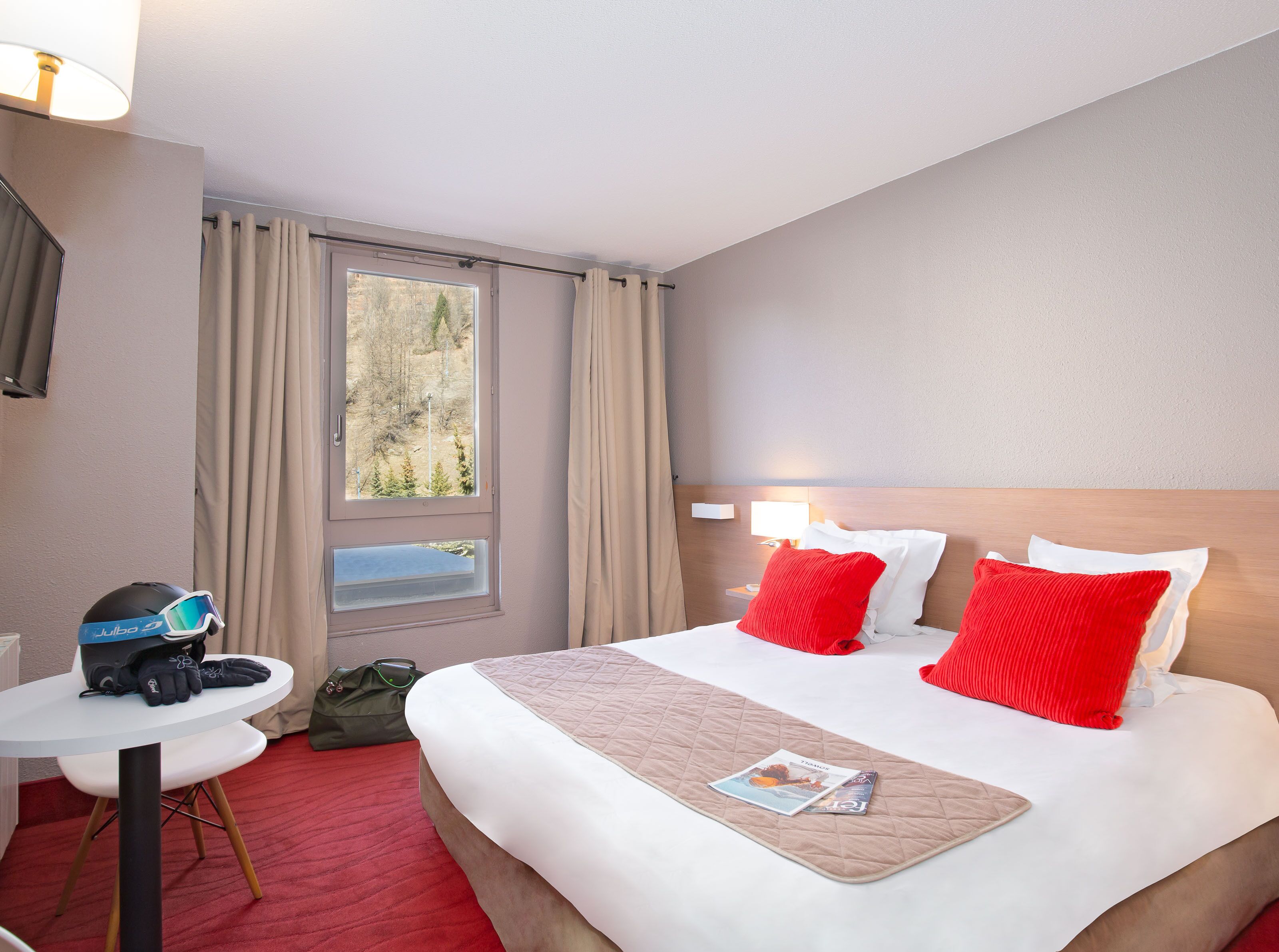 A hotel room with a bed, a bedside table, a window, and a view of trees.