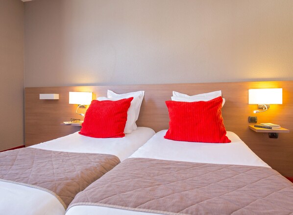 Habitación de hotel con dos camas, cada una con almohadas rojas y blancas, y mesitas de noche con lámparas.