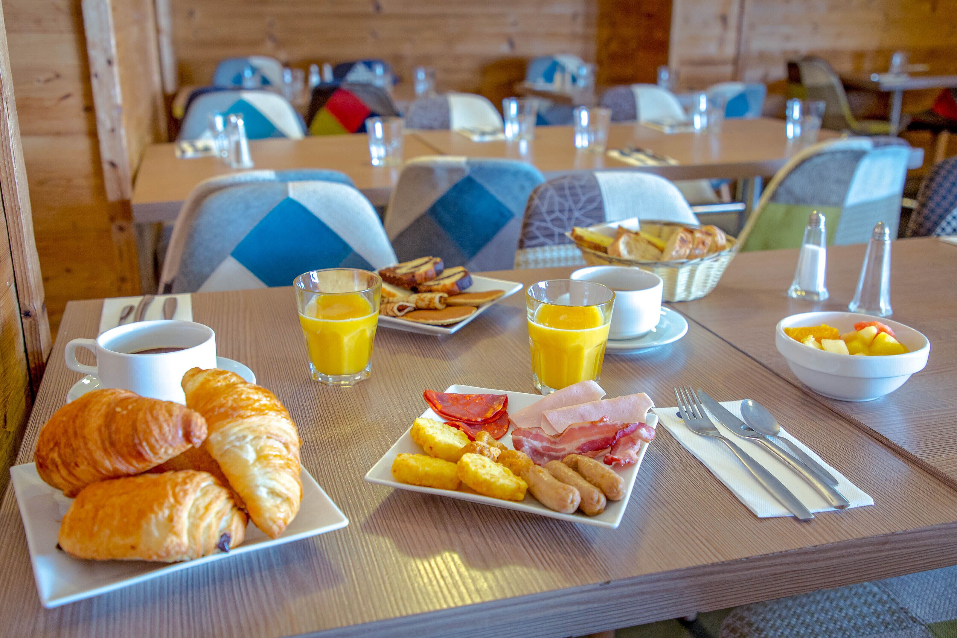 A breakfast table with croissants, eggs, bacon, and fruit.