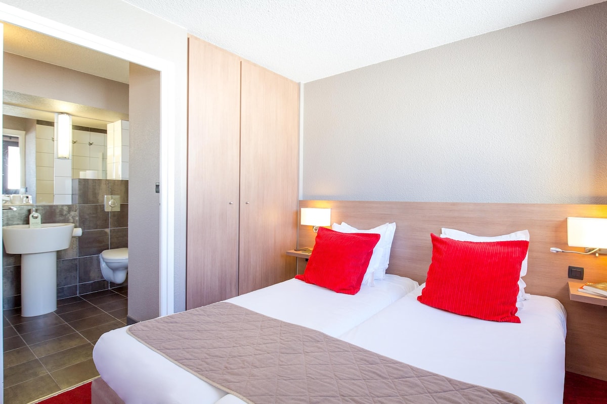 A hotel room with a large bed, two bedside tables with lamps, a wooden headboard, and a bathroom visible through an open door.