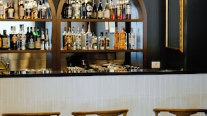 A bar area with three wooden bar stools, a tiled backsplash, and shelves stocked with various bottles. - c-hotels Club House Roma (Rome)