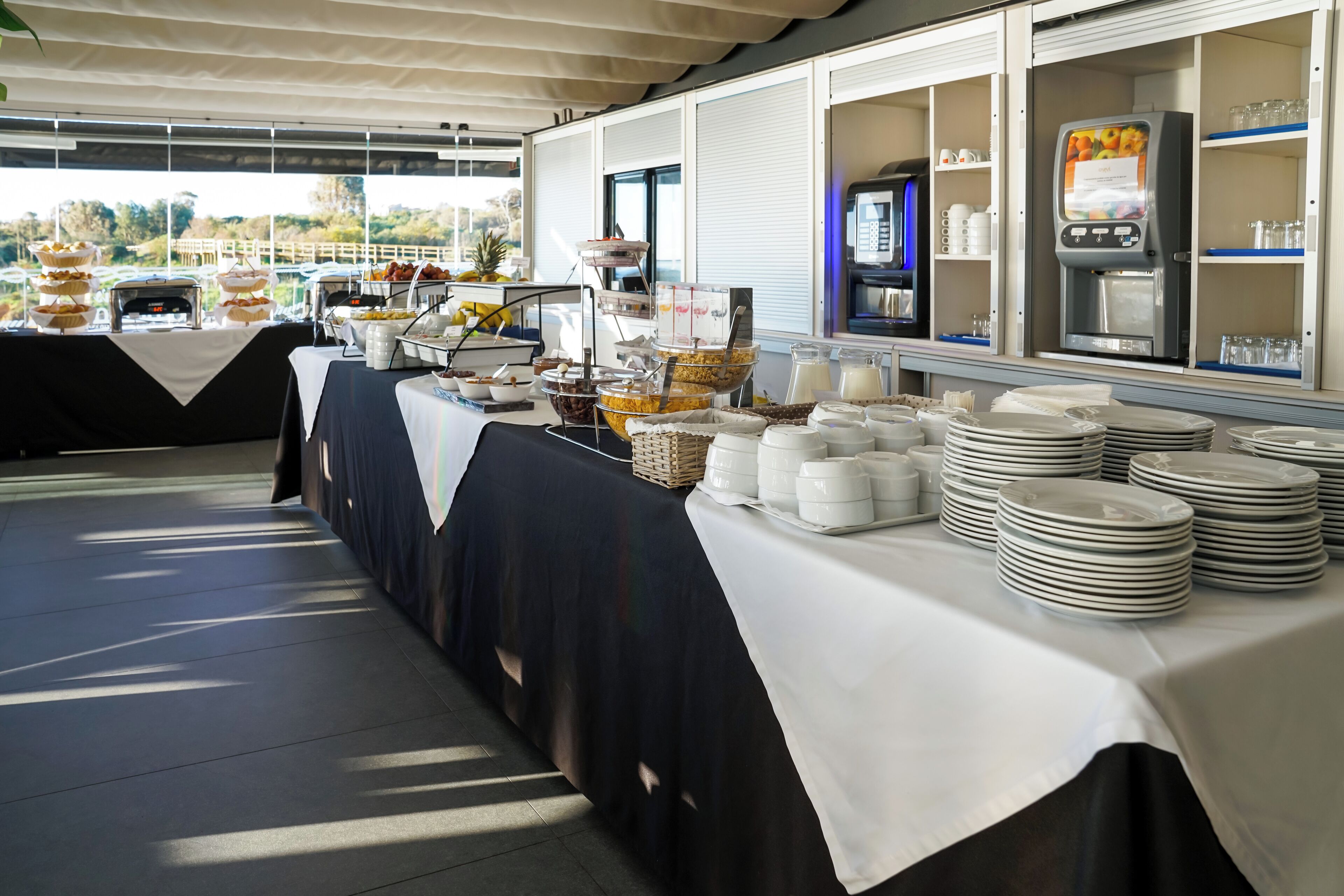 Un buffet proposant différents plats, une fontaine à boissons en libre-service et des assiettes soigneusement empilées.