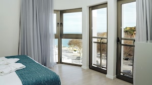 Un dormitorio con una cama, vistas al exterior a través de amplios ventanales correderos y un balcón.
