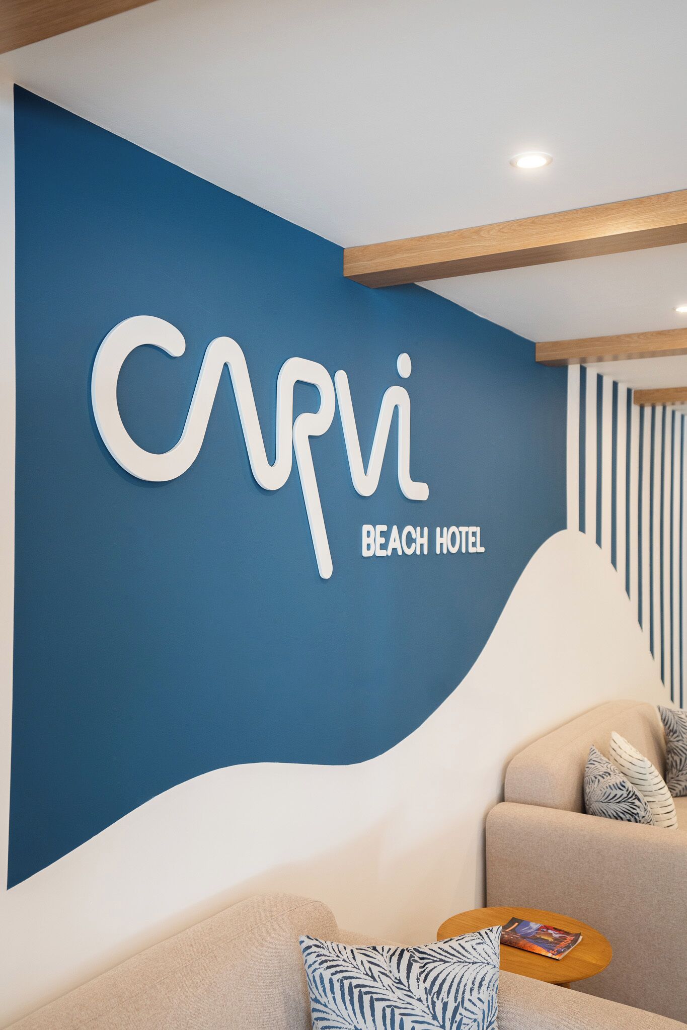 En blå væg med teksten "Capri Beach Hotel" og et moderne interiør med en sofa og et lille bord.