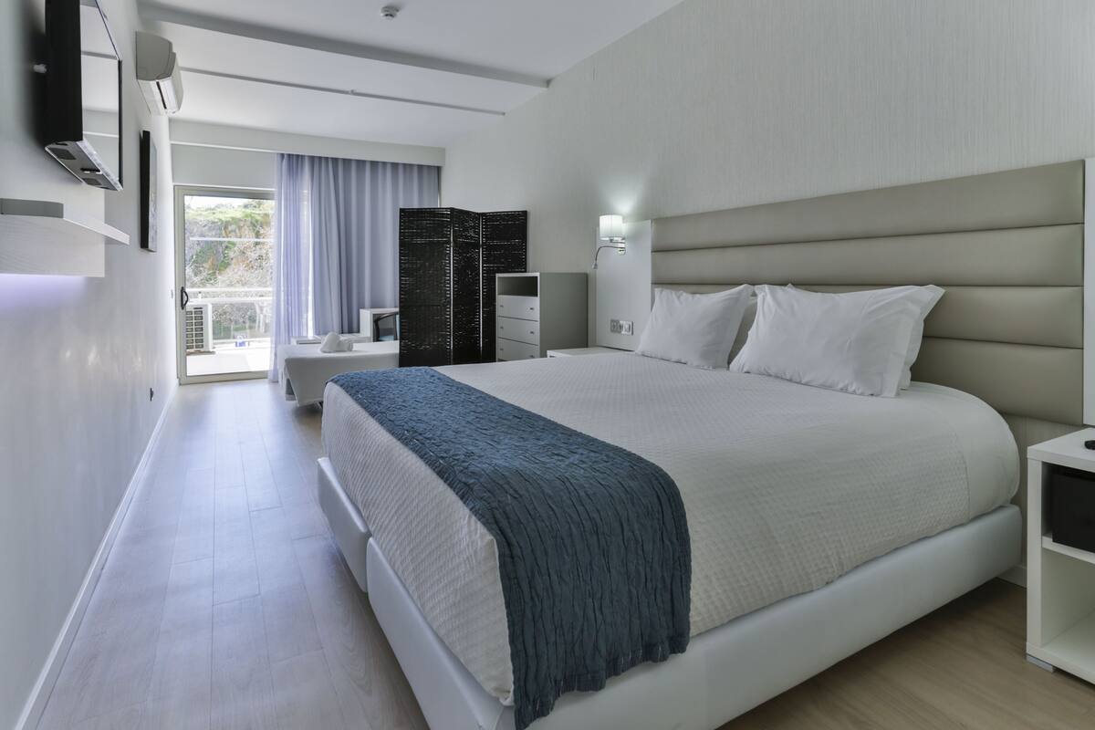 A modern hotel room with a large bed, a bedside table, a wardrobe, and a TV mounted on the wall.