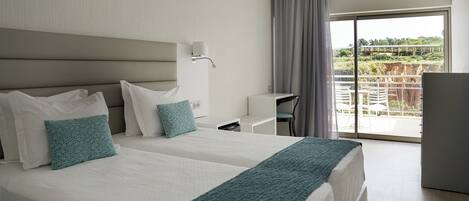 A hotel room with two beds, a desk, a chair, and a balcony with a view.