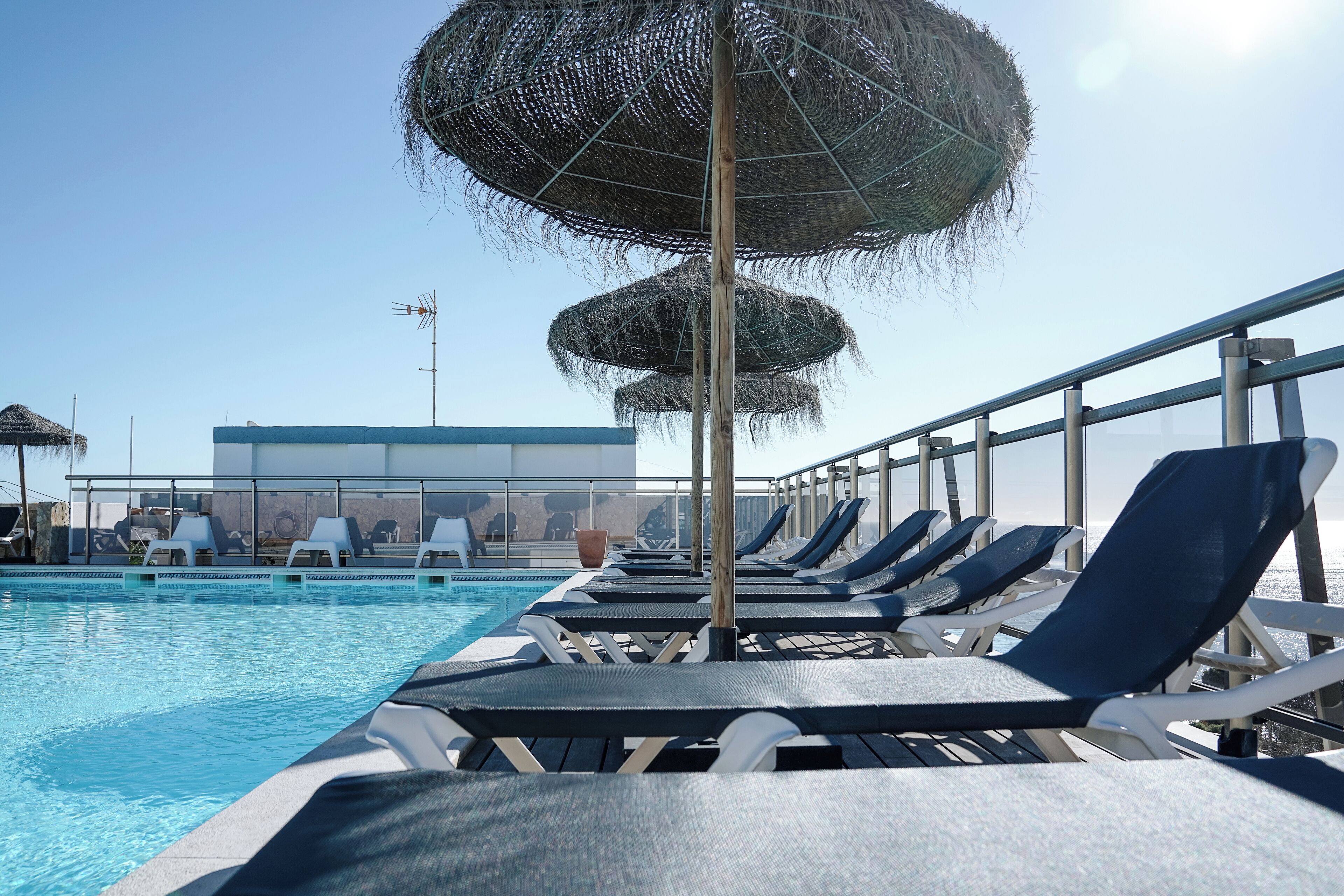 A poolside area with lounge chairs and thatched umbrellas.