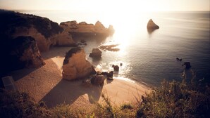 Un paisaje costero con acantilados rocosos, una playa arenosa y mar tranquilo.