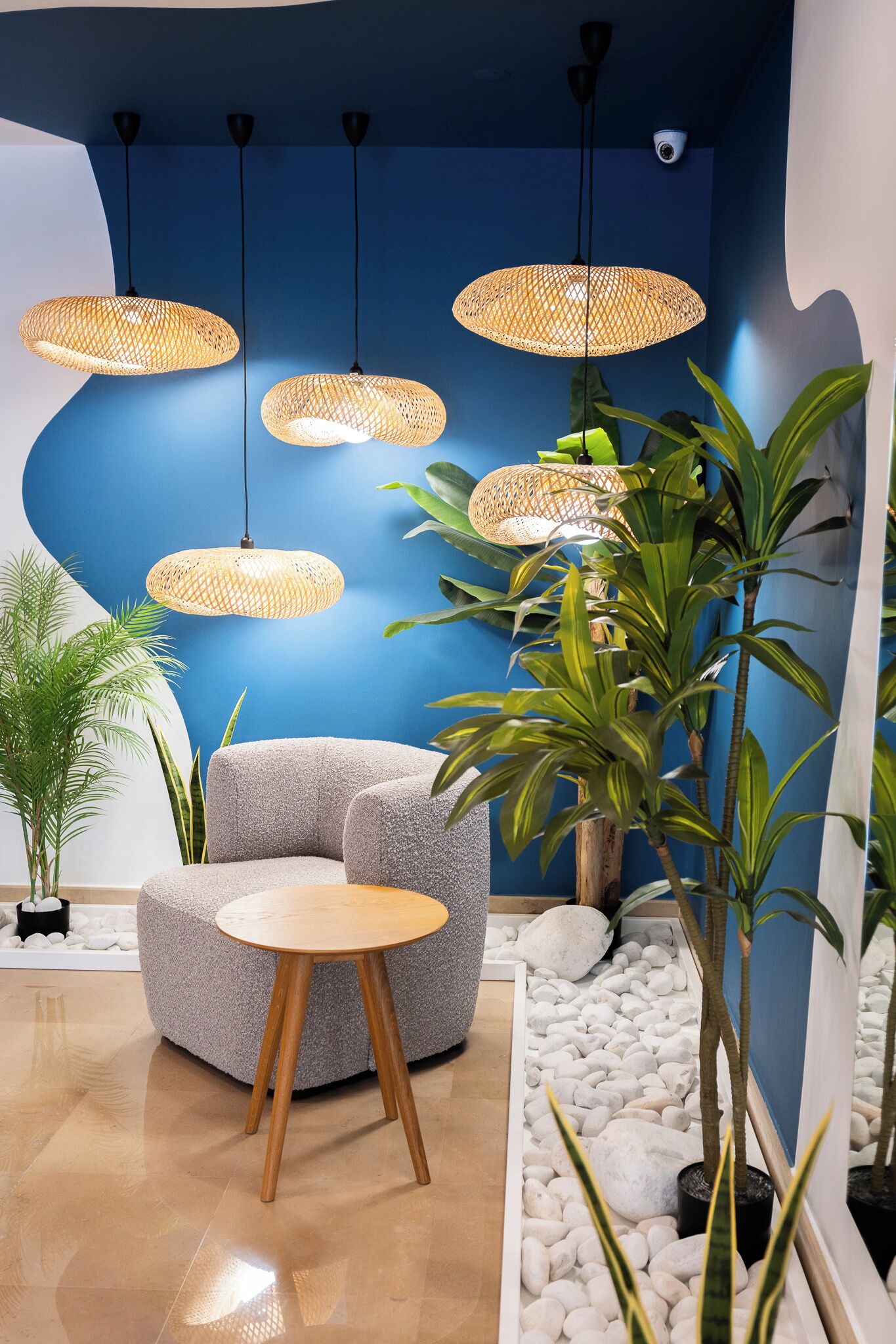 A modern interior with a blue accent wall, a round wooden table, a grey sofa, and multiple wicker pendant lights.