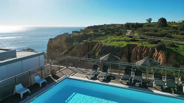 Una piscina con sillones de descanso y sombrillas, con vistas a un acantilado y al mar.
