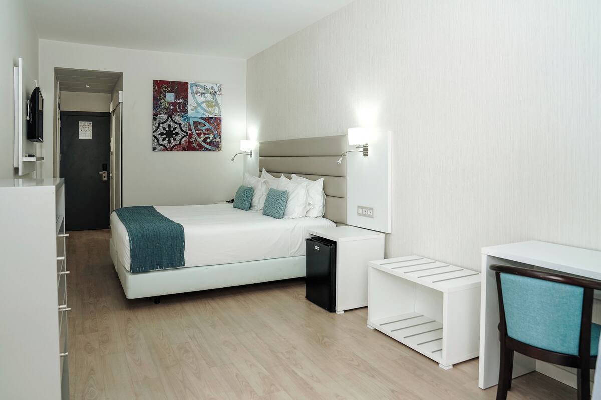 A modern hotel room with a bed, bedside tables, a desk, and a chair.