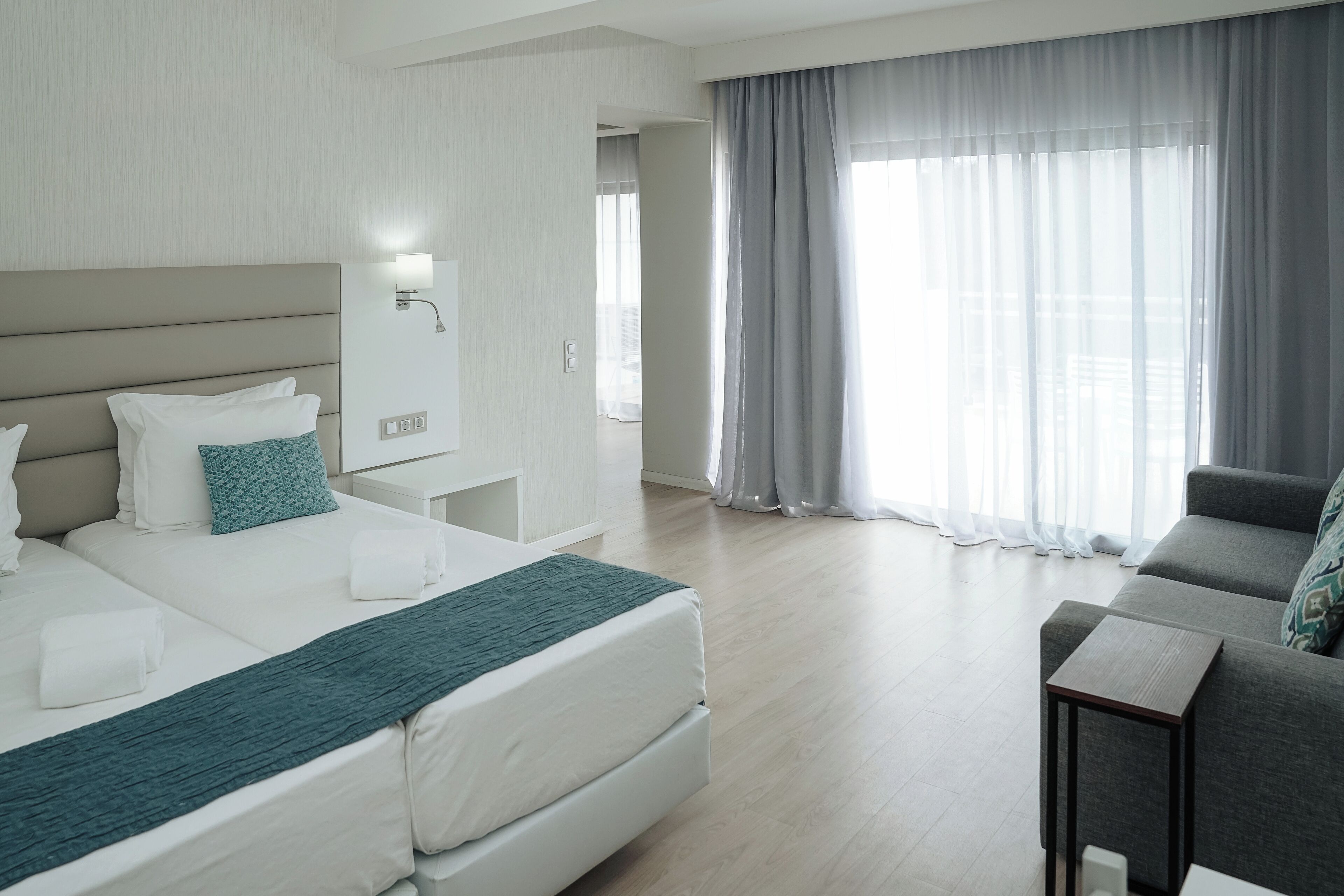 A hotel room with a large bed, a sofa, a nightstand, and a window with curtains.
