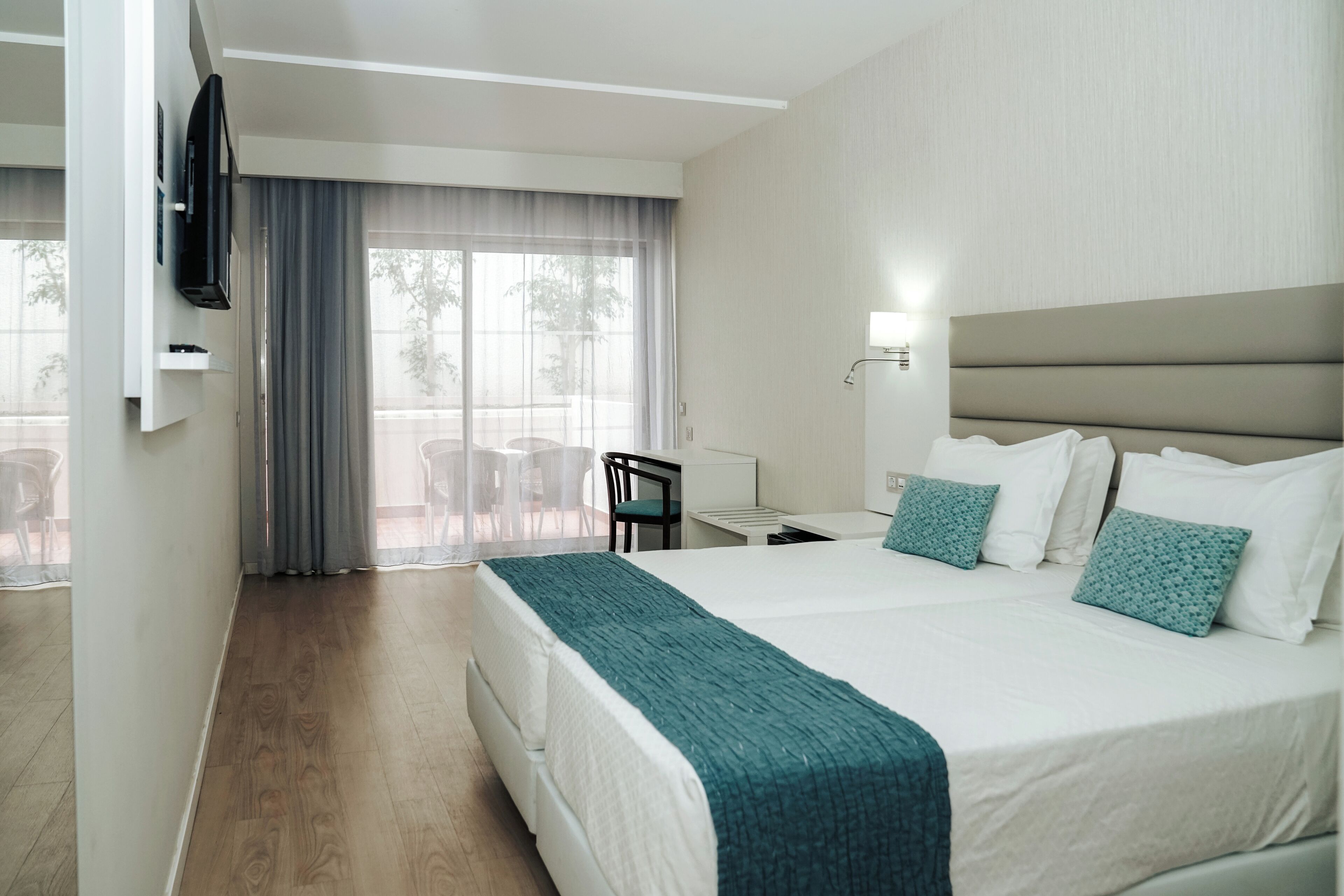 Una habitación de hotel con una cama grande, un escritorio, una silla, un televisor y una ventana con cortinas.
