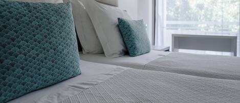 A neatly made bed with white and teal pillows, a textured white bedspread, and a bedside lamp.