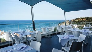 Un área de comedor al aire libre con mesas y sillas, con vista al océano.