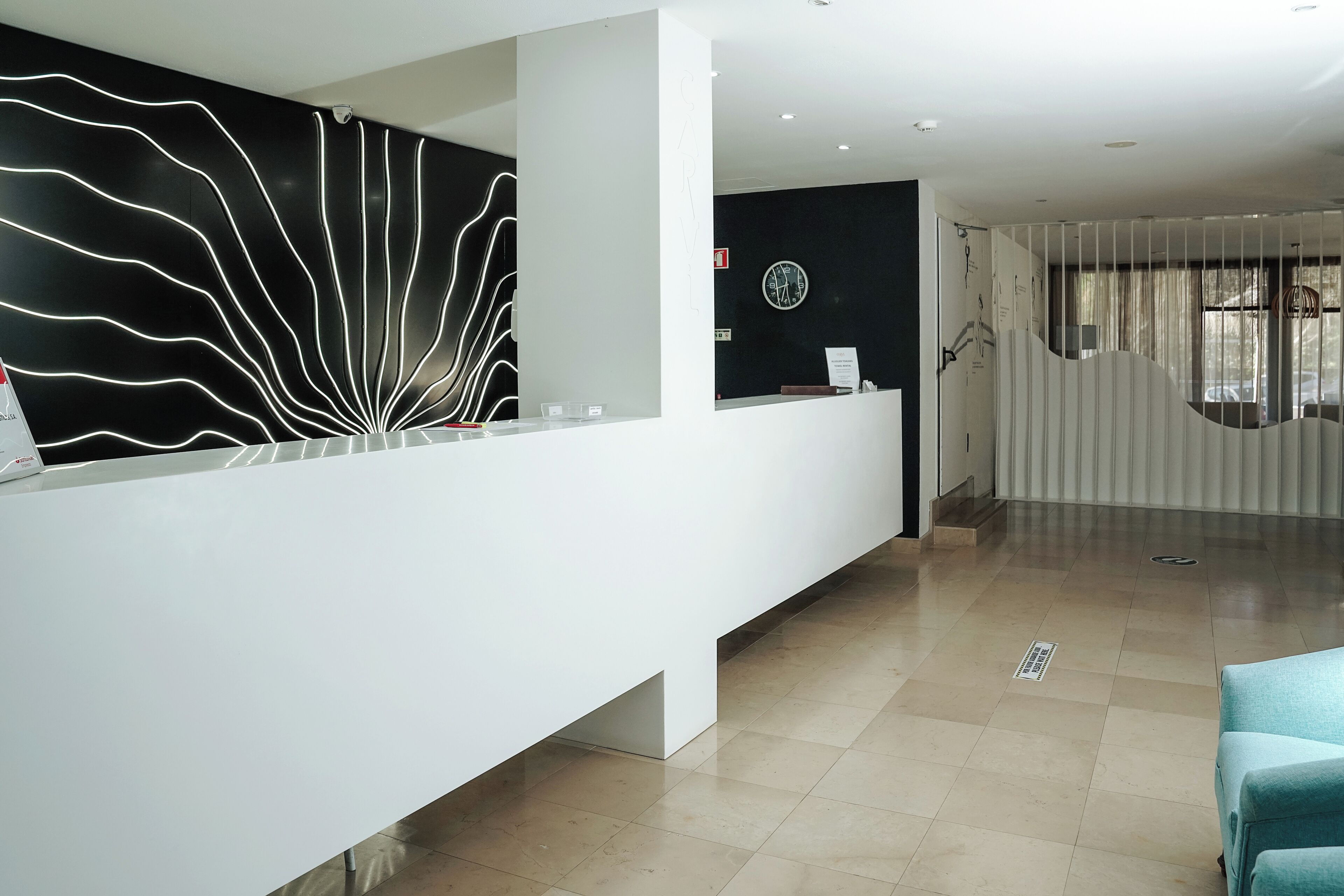 A modern reception area with a white reception desk, a black wall with white light patterns, and a large clock.
