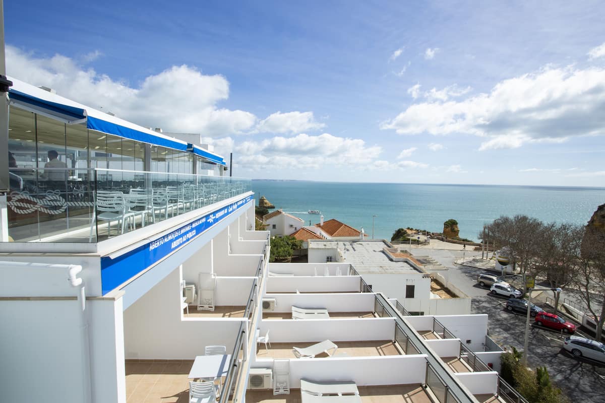 A rooftop terrace with white lounge chairs and a glass balustrade overlooking the sea.