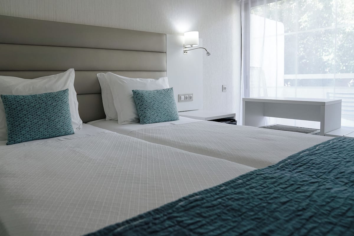 A modern hotel room with two beds, a nightstand, and a large window.