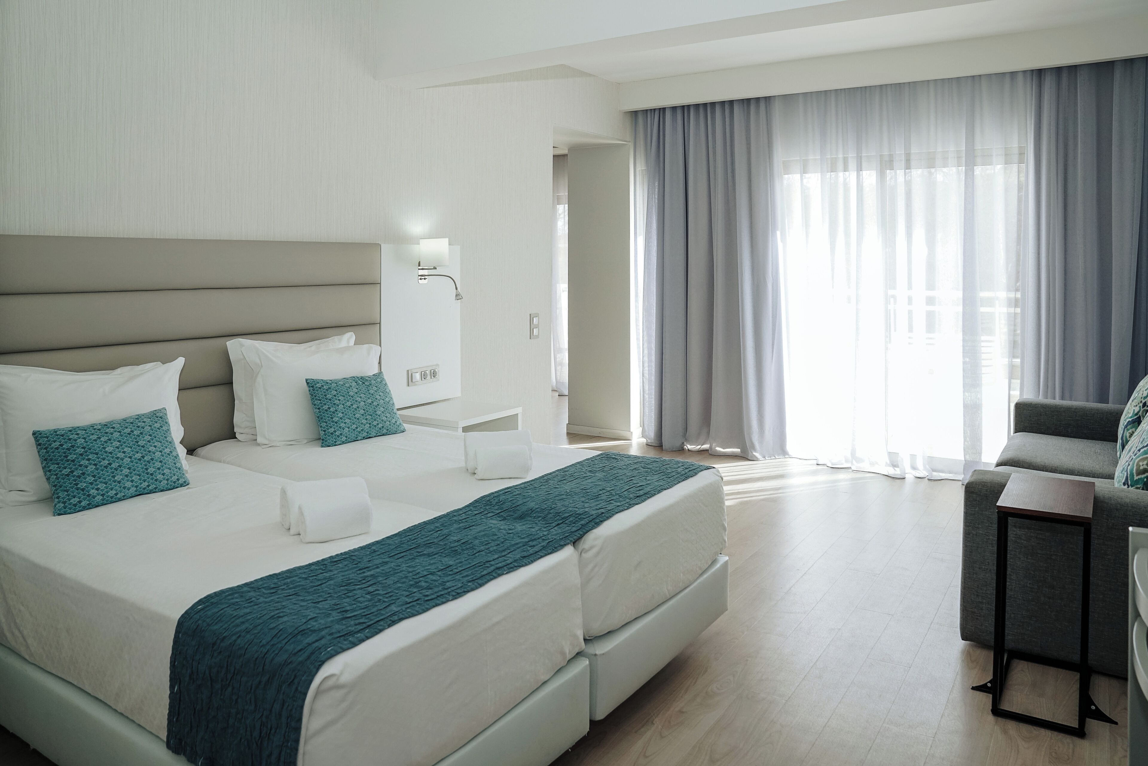 Une chambre d’hôtel moderne, dotée d’un grand lit, d’une table de chevet, d’une chaise et offrant une vue sur l’extérieur grâce à de grandes fenêtres.