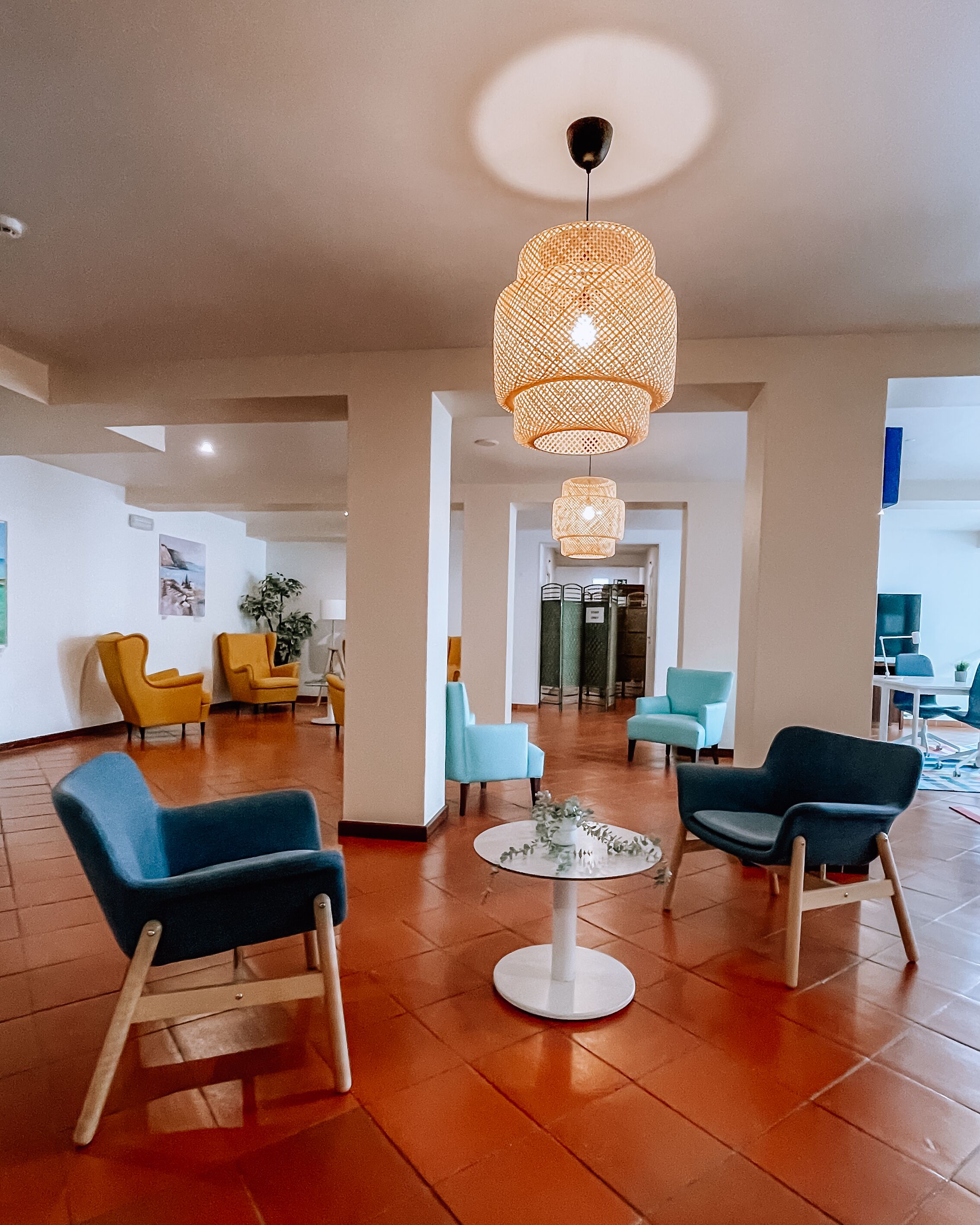 A spacious lobby with modern furniture, a central round table, and a distinctive woven light fixture.