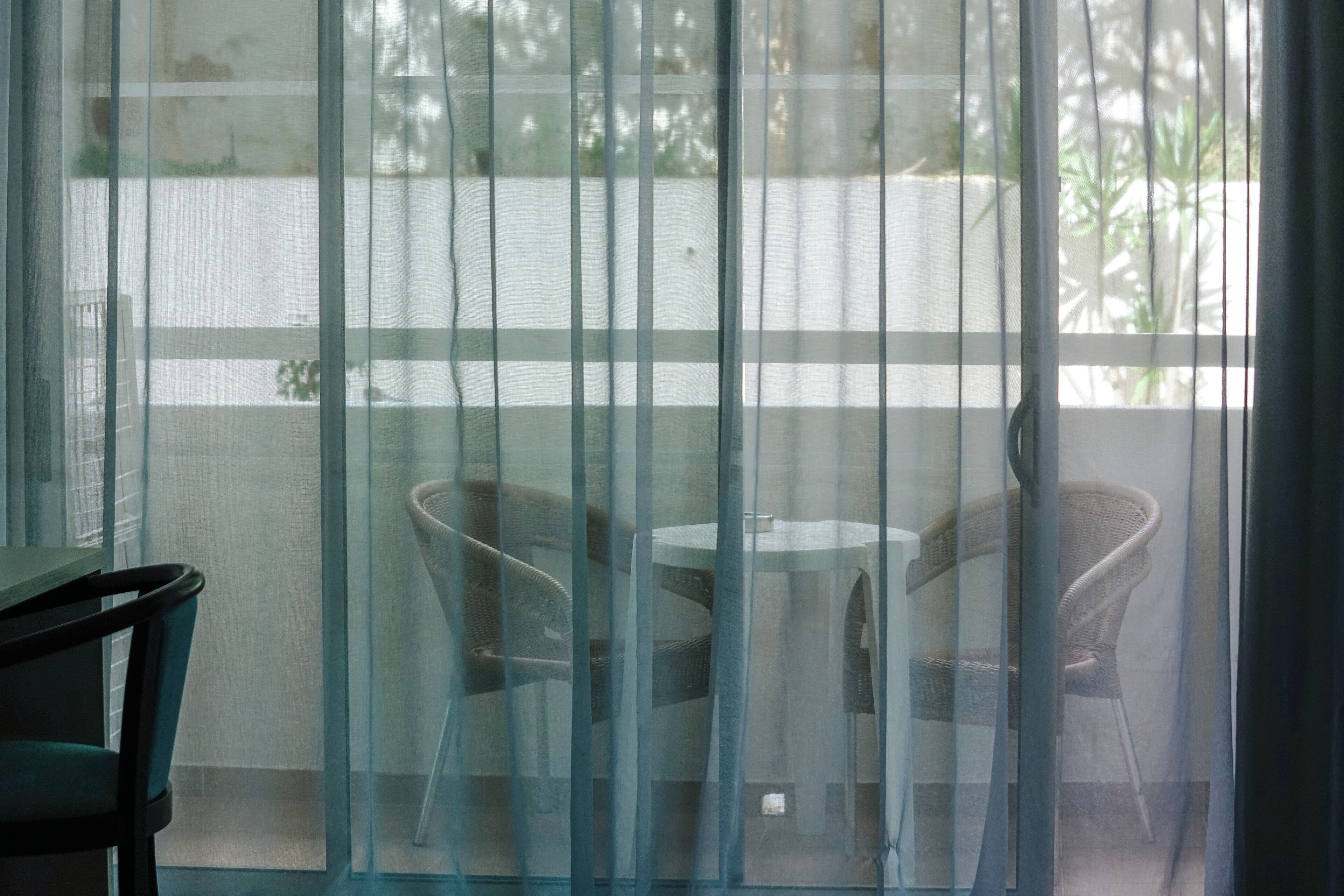 Una habitación con puerta de vidrio que da a un espacio exterior con dos sillas de mimbre y una mesita.