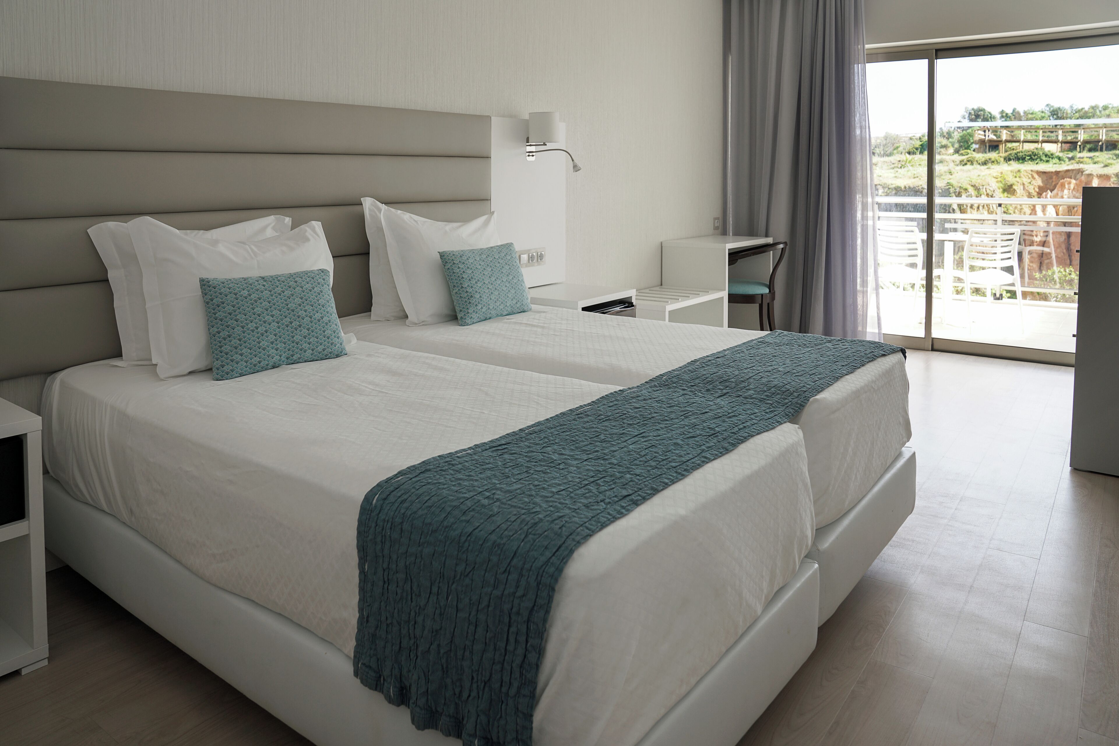 A modern hotel room with a large bed, a bedside table, a desk, and a view of the outdoors.