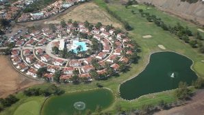 An aerial view of a resort with a central pool, multiple golf courses, and surrounding residential buildings. - eó Suite Hotel Jardin Dorado (San Bartolomé de Tirajana)