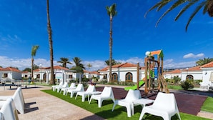 A resort with white lounge chairs, palm trees, and a playground. - eó Suite Hotel Jardin Dorado (San Bartolomé de Tirajana)