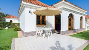 A white building with a tiled roof, a patio with a table and chairs, and a well-maintained lawn. - eó Suite Hotel Jardin Dorado (San Bartolomé de Tirajana)