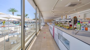A modern hotel lobby with a pool view, a buffet area with various food options, and a seating area with tables and chairs. - eó Suite Hotel Jardin Dorado (San Bartolomé de Tirajana)