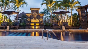A pool area with lounge chairs and umbrellas, surrounded by palm trees and stone pillars. - Taman Harum Cottages (Mas)