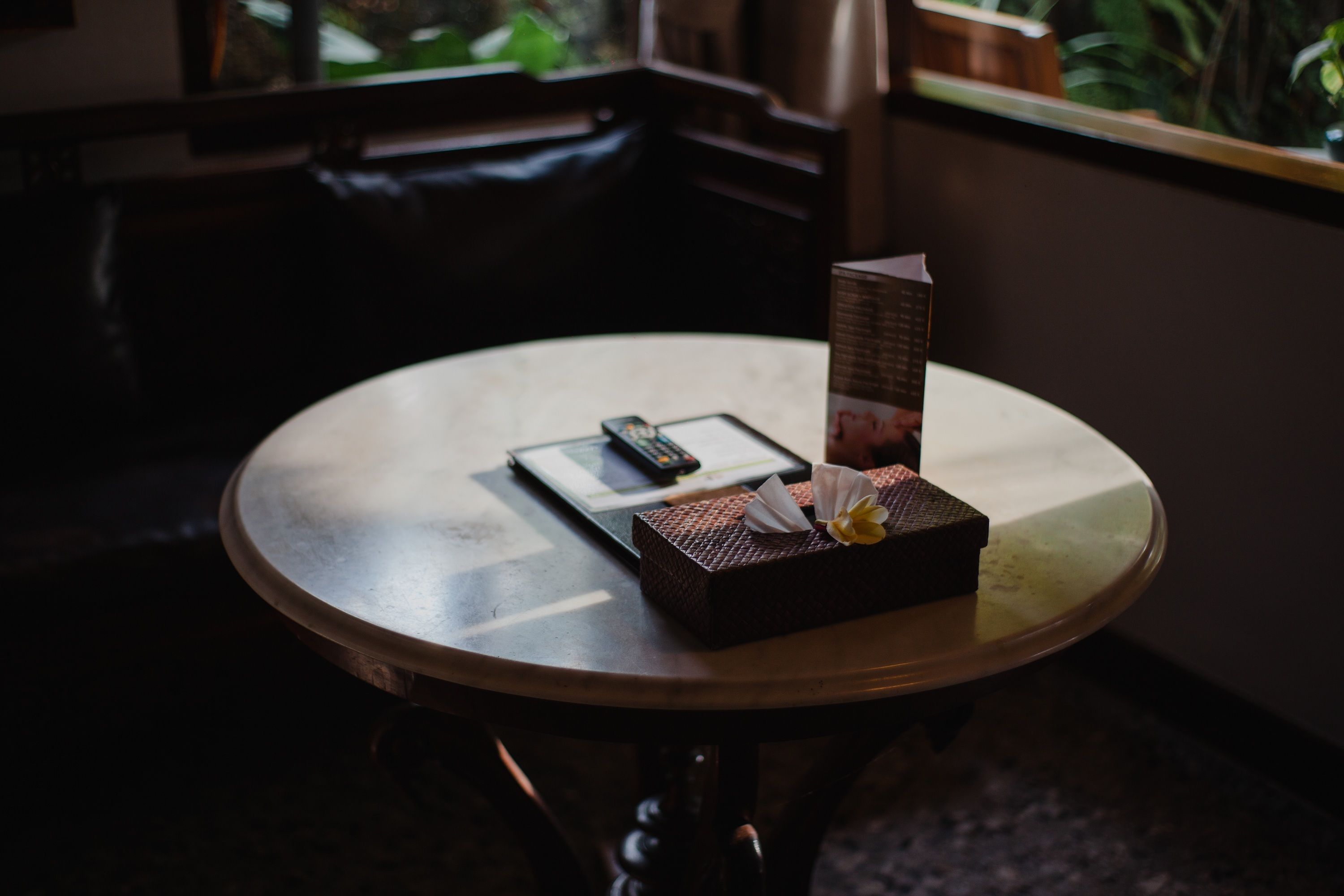 A round table with a remote control, a menu, and a small box with a napkin and a flower.