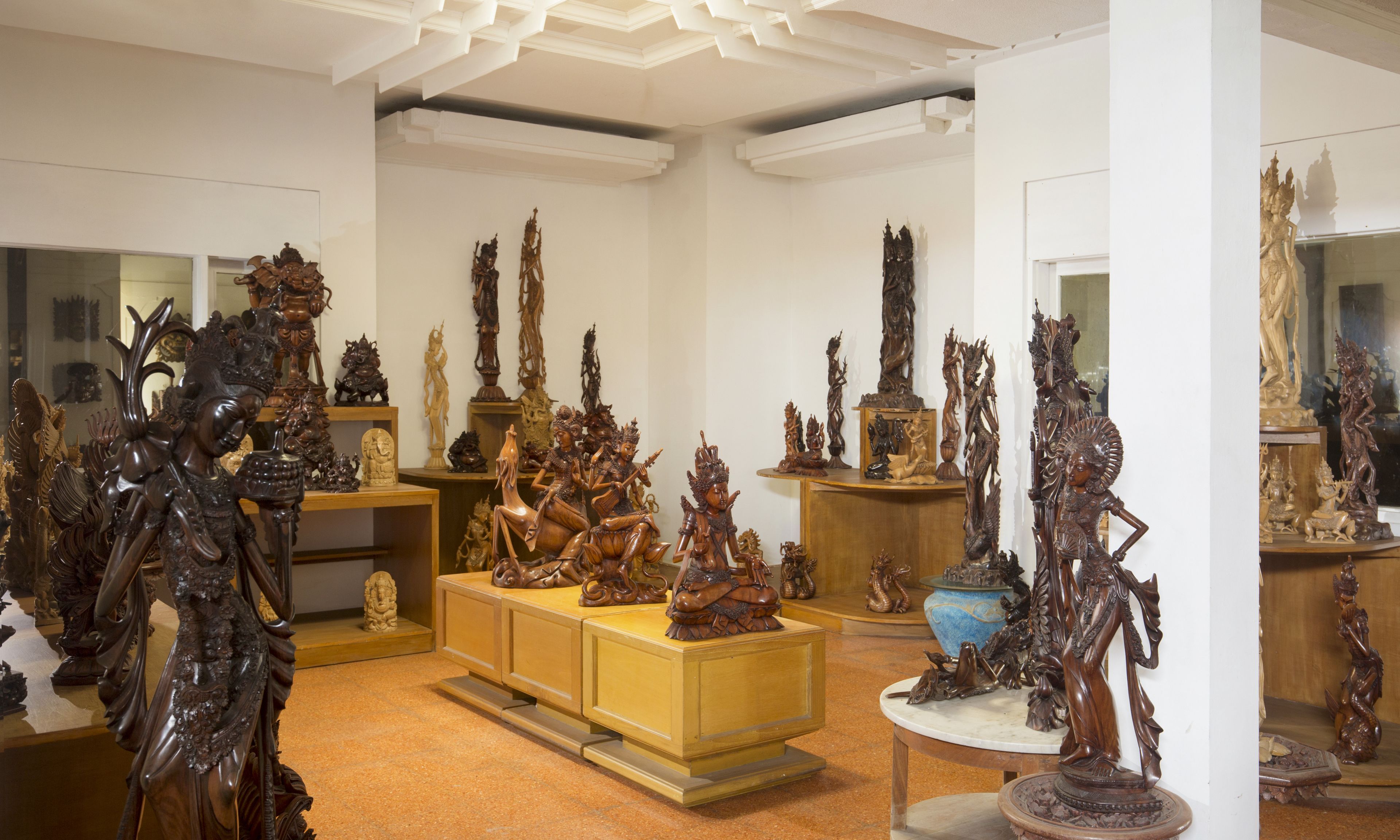 A room with multiple wooden sculptures and carvings displayed on shelves and tables.