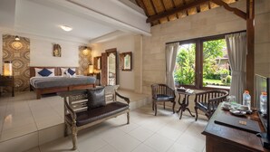A room with a bed, a sofa, a dining table, and chairs. There is a window with curtains and a view of greenery outside. - Taman Harum Cottages (Mas)