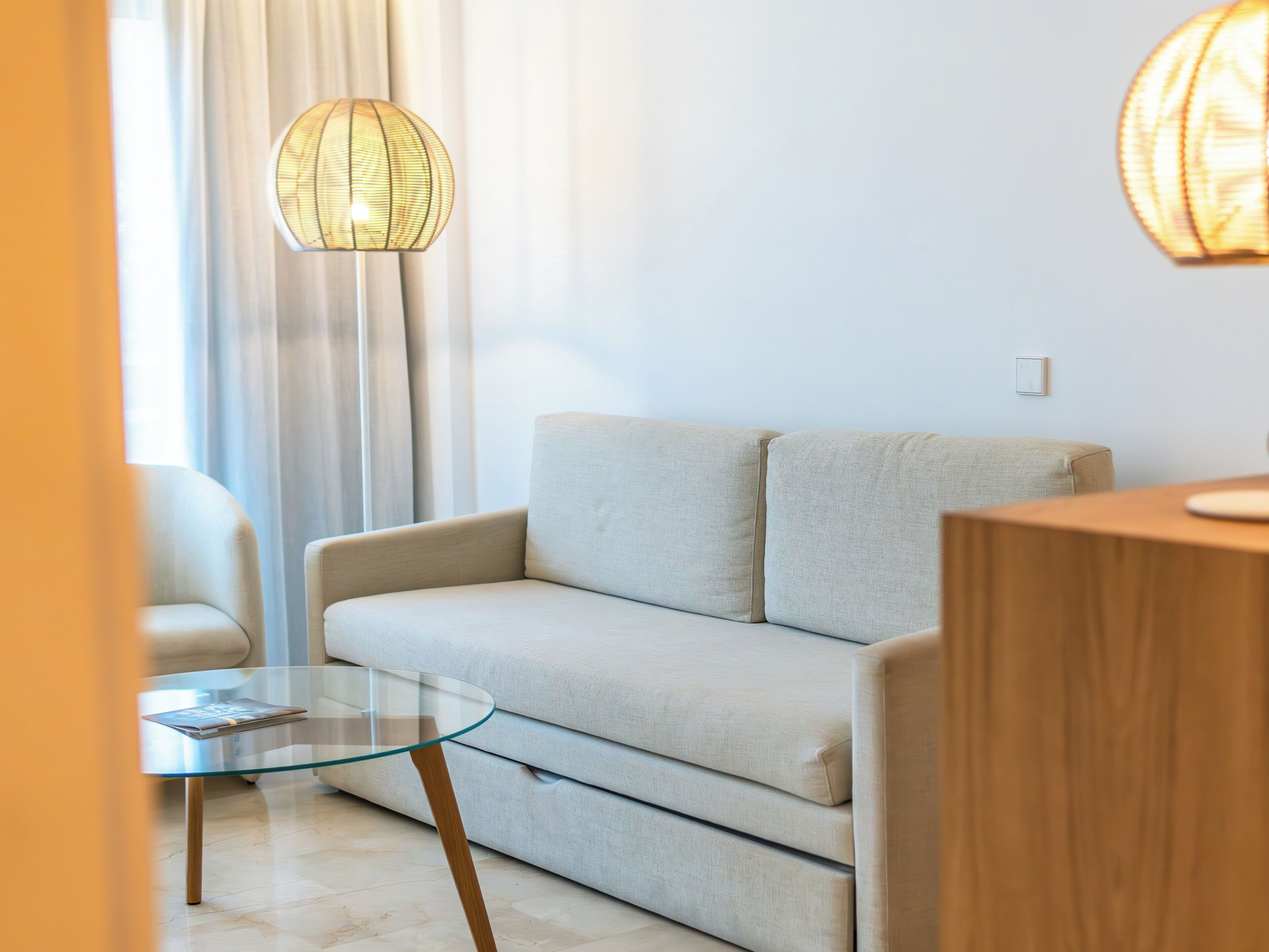 A modern living room with a sofa, a glass coffee table, and a hanging light fixture.