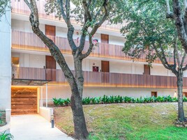 A multi-story building with balconies, a covered entrance, and a landscaped garden area.