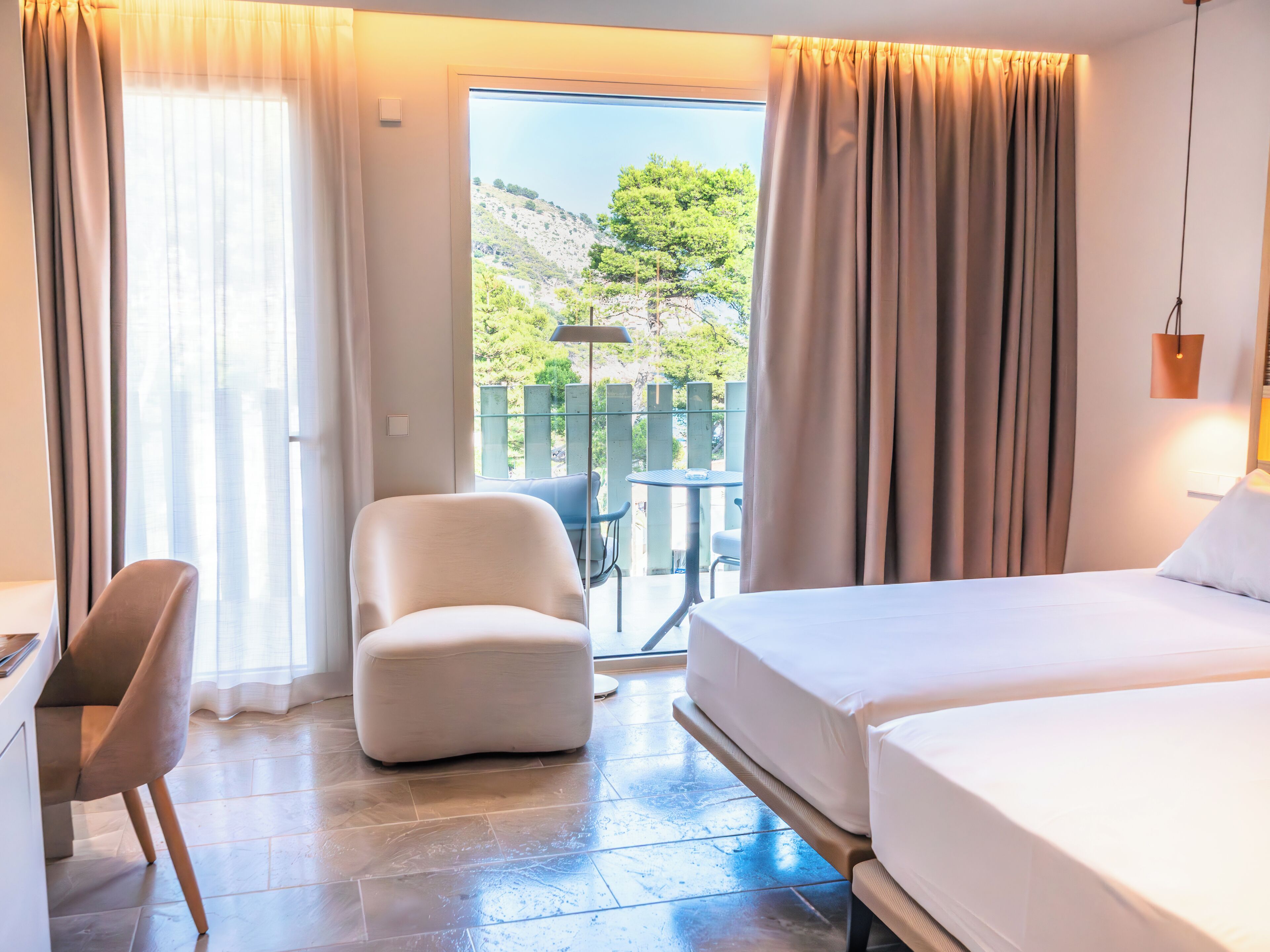 Une chambre d’hôtel avec un lit, une chaise, un bureau et une vue sur un balcon équipé d’une table et de chaises.