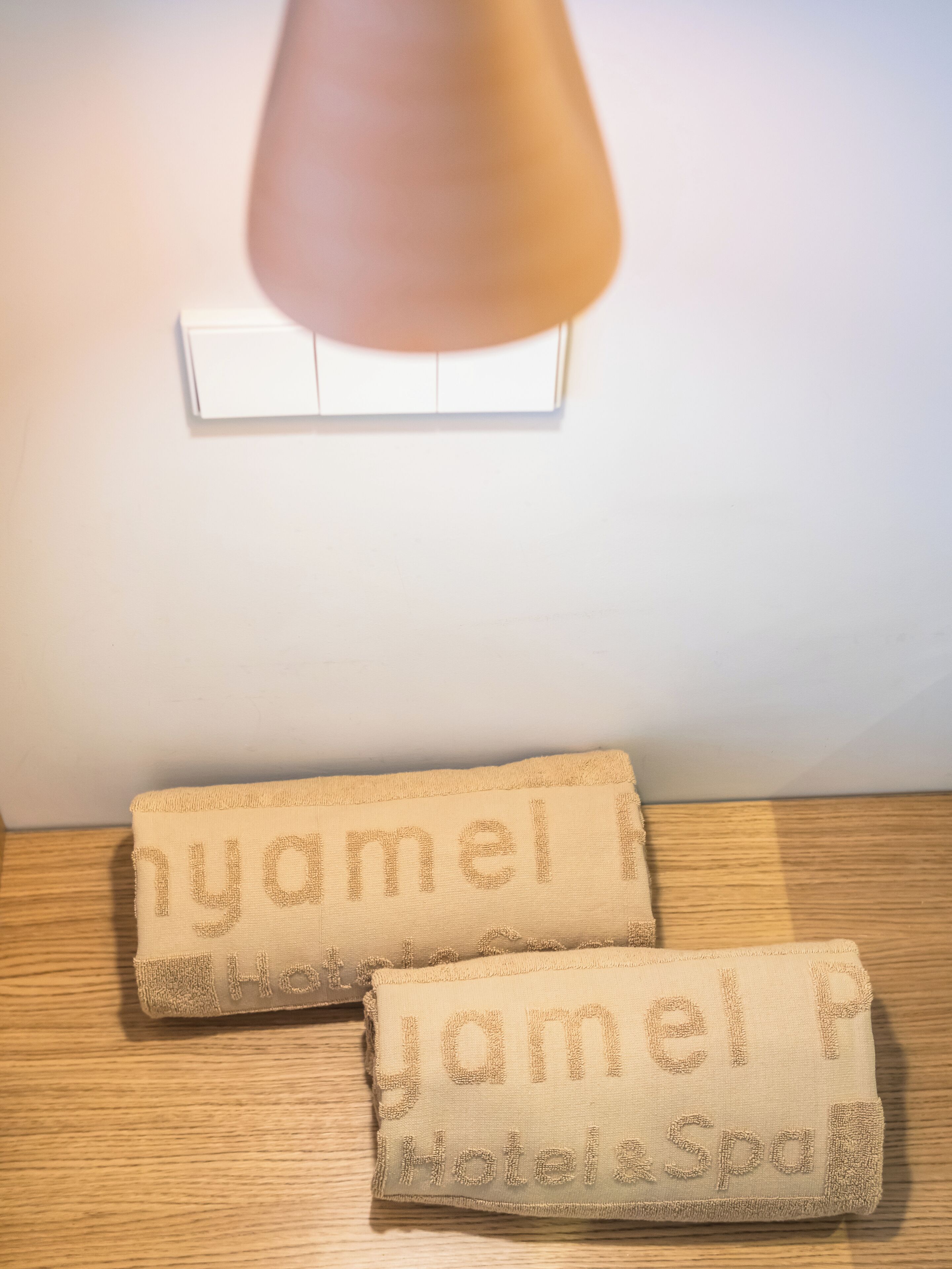 Two towels with embroidered text on a wooden surface, a light switch, and a wall in the background.