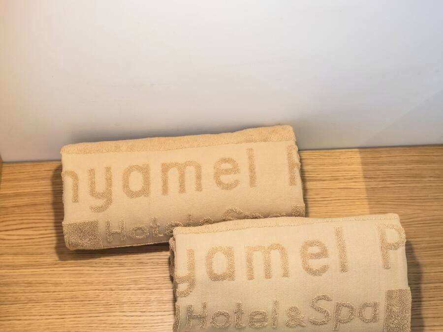Two towels with embroidered text on a wooden surface, a light switch, and a wall in the background.