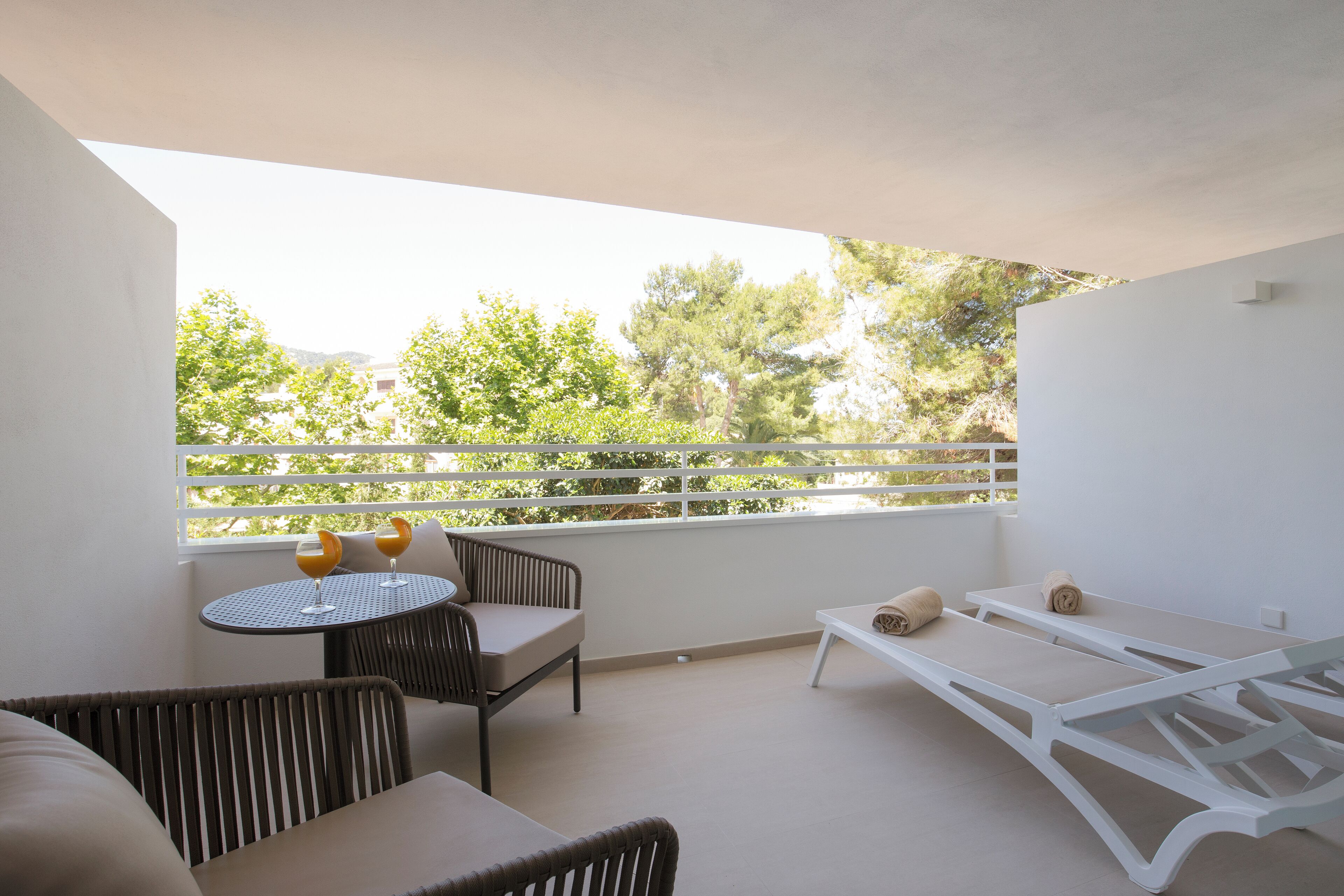 A balcony with a sofa, a small round table with glasses, and a sun lounger.